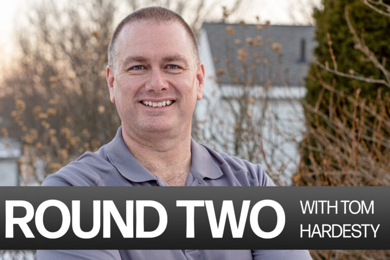 Head shot of Tom Hardesty, a white man with short hair in a grey golf polo with the caption "Round Two with Tom Hardesty"