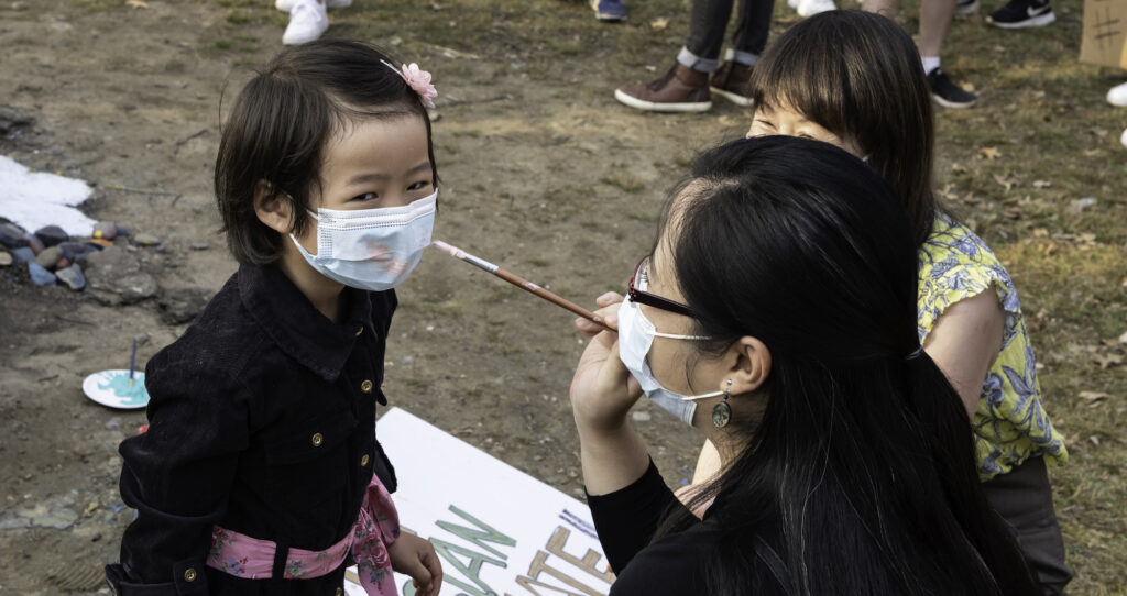 Image of a woman painting the surgical mask of a toddler