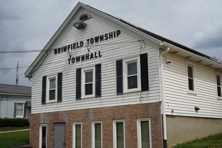 image of the brimfield town hall, a white siding and brick building, on a cloudy day