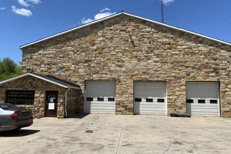 Image of Rivers Garage and Body Shop, a stone front building with three white garage doors