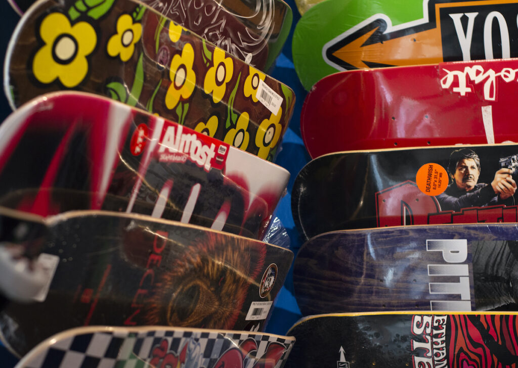 Photo of a wall of hanging skateboards. The boards are overlapping and cover the entire wall with vibrant colors and skate crew-type art.