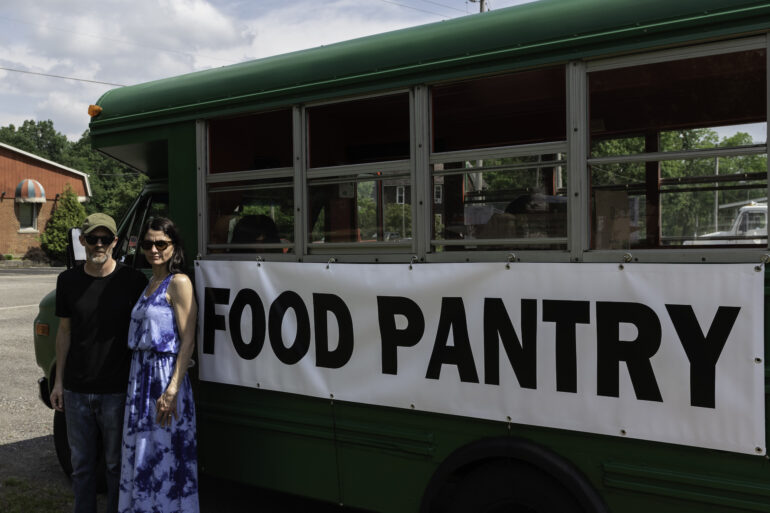 Image of two people standing in front of a green schoolbus with the words Food Pantry on the side