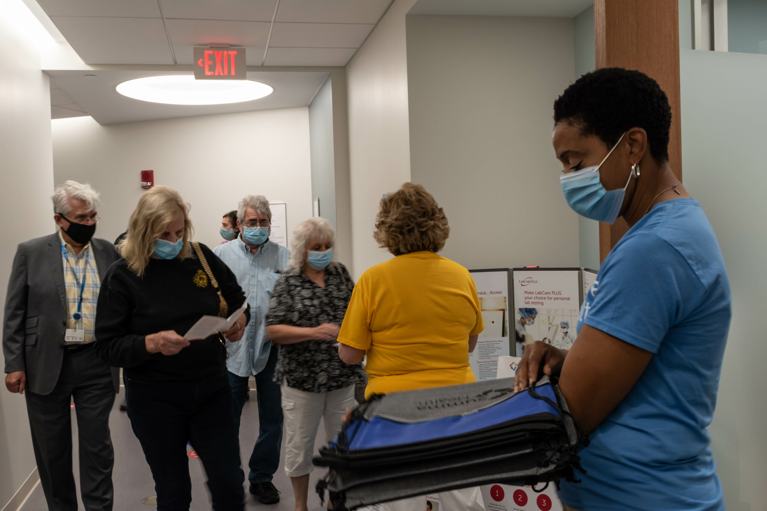 Photo of a woman in the foreground holding blue Summa Health drawstring bags, while a group of people pass through the area in the background. Everyone inn the photo is wearing a mask.