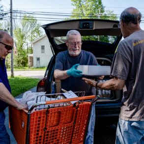 Photo of three men helping load grocerties in a parking lot