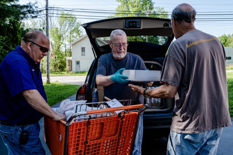 Photo of three men helping load grocerties in a parking lot