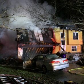 An image of a burning home with a car parked in the driveway at night with smoke billowing from the garage area