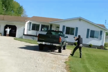 Image of a deputy moving toward a woman with his gun aimed at her while she is standing in the entryway of a garage