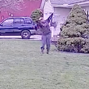 Image of a man standing on his lawn giving the middle finger toward his neighbor's house while holding a caged animal