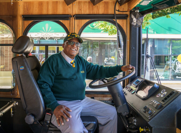 Image of a man sitting behind the will of a public bus that has been designed to look like a 19th century streetcar