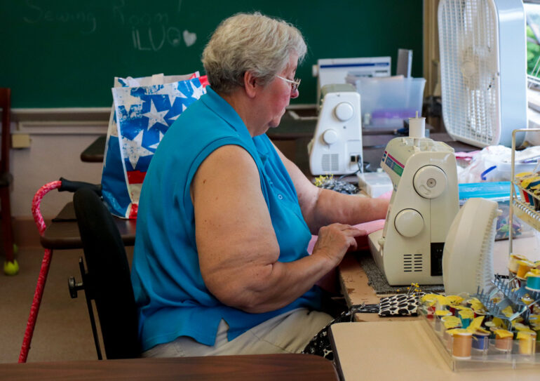 Image of a woman in a blue blouse sitting at a sewing machine in a classroom workshop