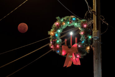 Image of a dark red moon framed by power lines and a holiday wreath