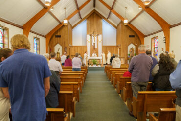 A scattering of parishioners gather in a well-lit church, with a row of clergy at the altar